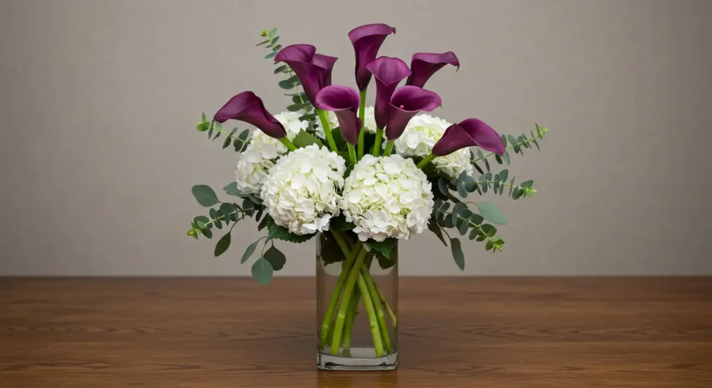 Elegant floral arrangement with purple calla lilies, white hydrangeas, and eucalyptus in a glass vase.